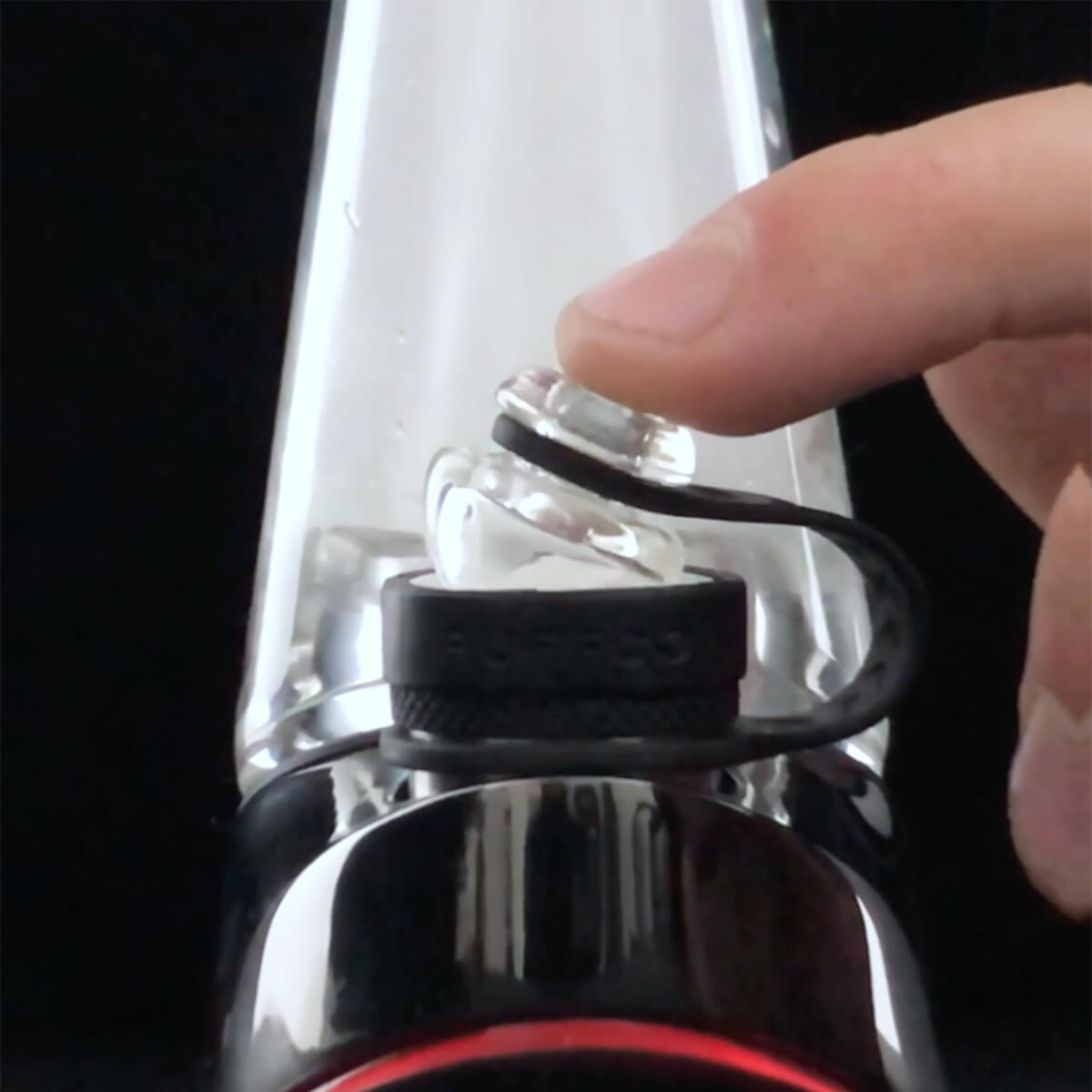 Hand operating glass carb cap on black dab rig against black backdrop